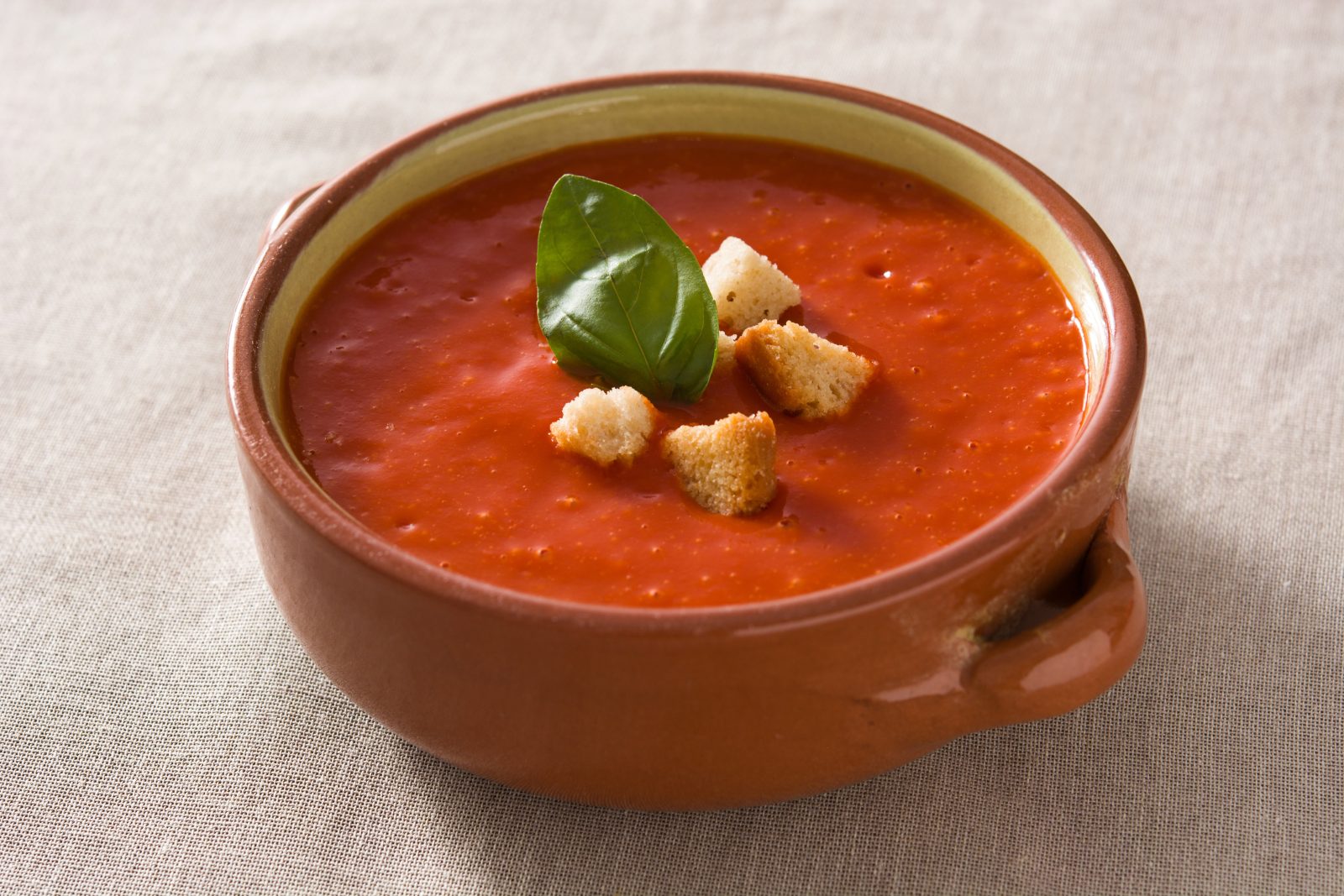 Une soupe de tomates au basilic servie dans un plat en terre cuite